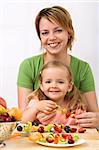Happy healthy woman and little girl making summer fruits kebab