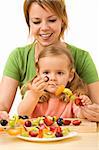 Woman and little girl preparing fruit slices on wooden sticks for a healthy snack - isolated