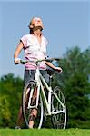 Pretty girl standing with a bicycle and enjoing the sun