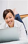 Attractive Asian woman lying down and smiling while working on a laptop. Vertically framed photo.