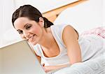 A beautiful young woman using a laptop in bed.  She is smiling at the laptop screen. Horizontally framed shot.