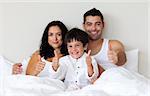 Young smiling family lying together on bed