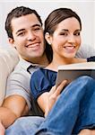 An attractive young couple relaxing together.  The female is holding a book and they are smiling directly at the camera. Vertically framed photo.