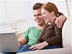 A young and attractive couple sitting together and viewing a laptop screen. They are smiling and laughing. Horizontally framed photo.