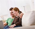 A couple sitting together and viewing a laptop screen. They are smiling. Horizontally framed photo.