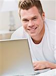 An attractive young man smiling and using a laptop.  Vertically framed shot.
