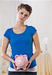 A young female holding a piggy bank.  She is facing the camera and has a worried look on her face. Vertically framed photo.