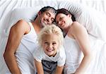 Happy little girl on bed with her parents smiling at the camera