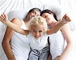 Happy little girl on bed with her parents in the morning