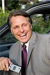 A happy laughing forties businessman is sitting in his car and laughing while holding his cellphone.