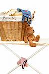 Teddy bear with laundry basket on ironing board against white background