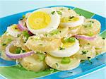 A plate of potato salad layered with hard-boiled eggs and red onions.