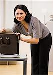 Attractive brunette searching in briefcase, looking at camera. Vertical