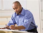 A young businessman is working on some blueprints in an office.  He is looking away from the camera.  Horizontally framed shot.