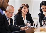 A group of business people are seated around a desk in a meeting.  They are looking away from the camera.  Horizontally framed shot.