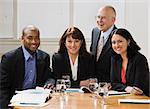 Four business workers, two men and two women, sitting at desk smiling at camera. Horizontal