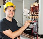 Young apprentice electrician measures power coming through coils of an industrial power distribution center.