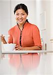 A woman is eating a bowl of rice at the kitchen table and smiling at the camera.  Vertically framed shot.