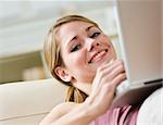 A young woman is using a laptop and smiling at the camera.  Horizontally framed shot.