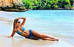 Blond girl in sunglasses lying on the beach with reflection in water