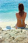 Beautiful brunette with long hair in white hat and swimsuit sits on the sand ocean beach on Bali in Indonesia