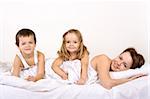 Happy kids and woman posing for a family portrait in bed