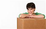 A beautiful young brunette posing while resting her arms on a cardboard box.  She is smiling directly at the camera. Horizontally framed shot.