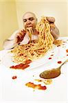 An overweight bald man enjoying a plate of spaghetti.  Shot with fish-eye lens.  Focus is on the face.