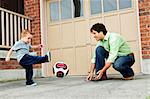 Father teaching son to play soccer on driveway