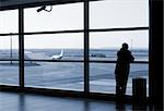 Airport lounge or waiting area with business man standing looking outside of window towards control tower