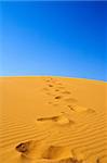 footsteps on sand dunes, cloudless sky in background