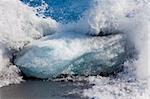 Langsame Shuttersped Schuss einer Welle brechen gegen einen Eisberg auf einem schwarzen vulkanischen Sandstrand in Island.