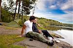 A man and woman happy camping in the forest by a lake