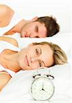 Attractive couple in bed with alarm clock and woman smiling at the camera
