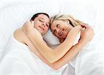 Couple lying together in bed and smiling at the camera