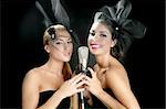 Beautiful women couple singing on a vintage microphone on black background