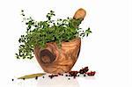 Thyme herb leaves in an olive wood  mortar and pestle, with star anise spice, peppercorns and a bay leaf, over white background.