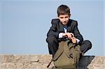 a successful school student is sitting on the stones and holding his schoolbag in his hands