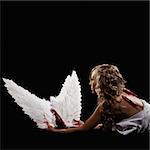 A young, adult female model is lying down and draped in white fabric. She is in profile, looking away from the camera and viewable from the waist up. She is holding wings that she has taken from her back as indicated by bloody back wounds. The shot is in a square format.