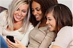 Three beautiful young women having fun looking at something funny on their smart cell phone and laughing