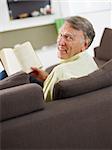 senior man reading book at home and looking over shoulders
