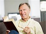 senior man reading book at home and looking at camera. Copy space