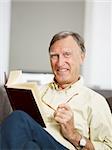 senior man reading book at home and looking at camera. Copy space