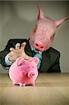 A piggy bank with a businessman wearing a (pig) mask about to grab it!