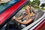 A beautiful young blond woman driving her convertible car and talking on her cell phone with a bluetooth headset