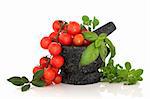 Herb leaf selection of oregano, basil and bay leaves with cherry tomatoes  in a granite mortar with pestle, over white background.