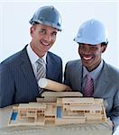 Smilingengineers with hard hats holding a model house and blueprints