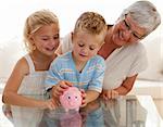 Smiling grandmother and children saving money in a piggybank