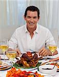 Smiling man eating turkey in Christmas dinner with his family