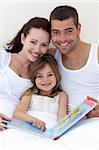 Portrait of parents and daughter reading together in bed